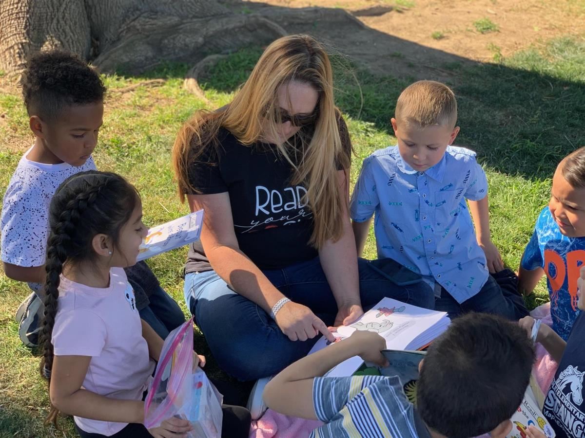 teacher in grass with children reading